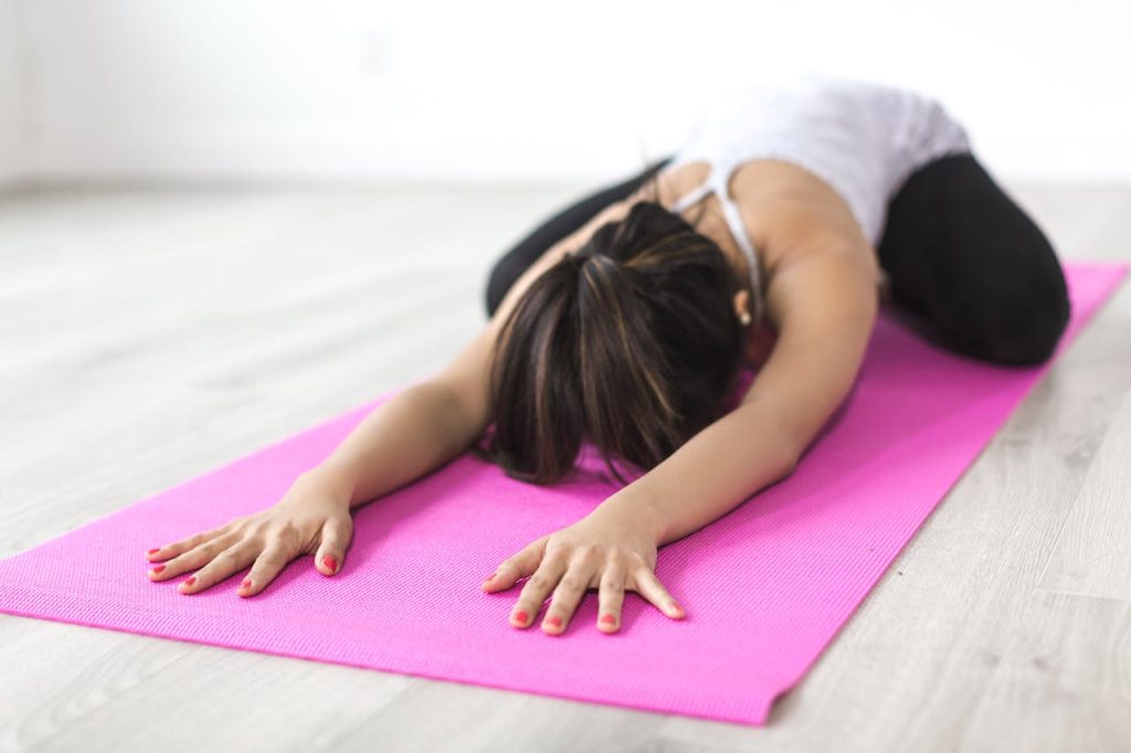 Adult woman practicing yoga in childs pose on pink mat indoors, focusing on relaxation and mindfulness.